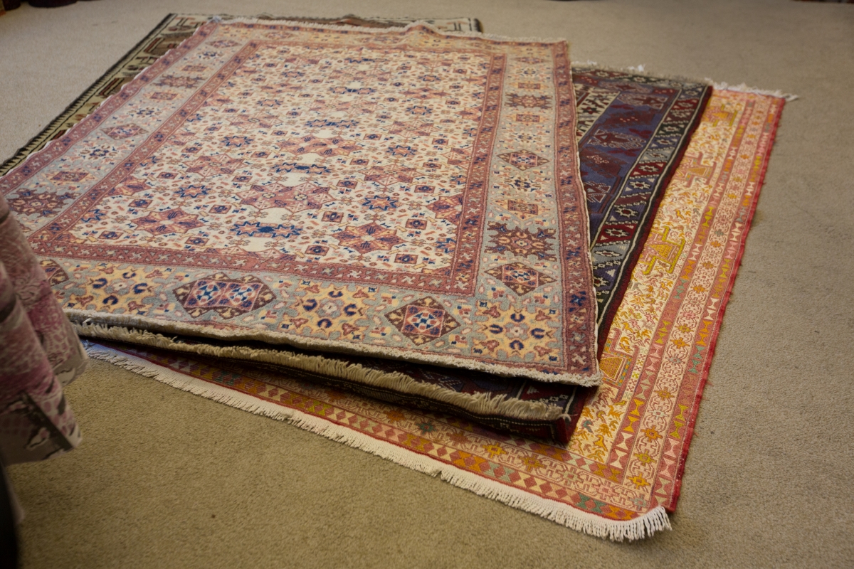 Multiple Turkish rugs layered on top of each other on a concrete floor.