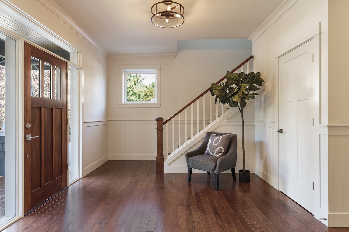 An entryway with dark hardwood floors dow not have an entry mat, but features an armchair and tree.