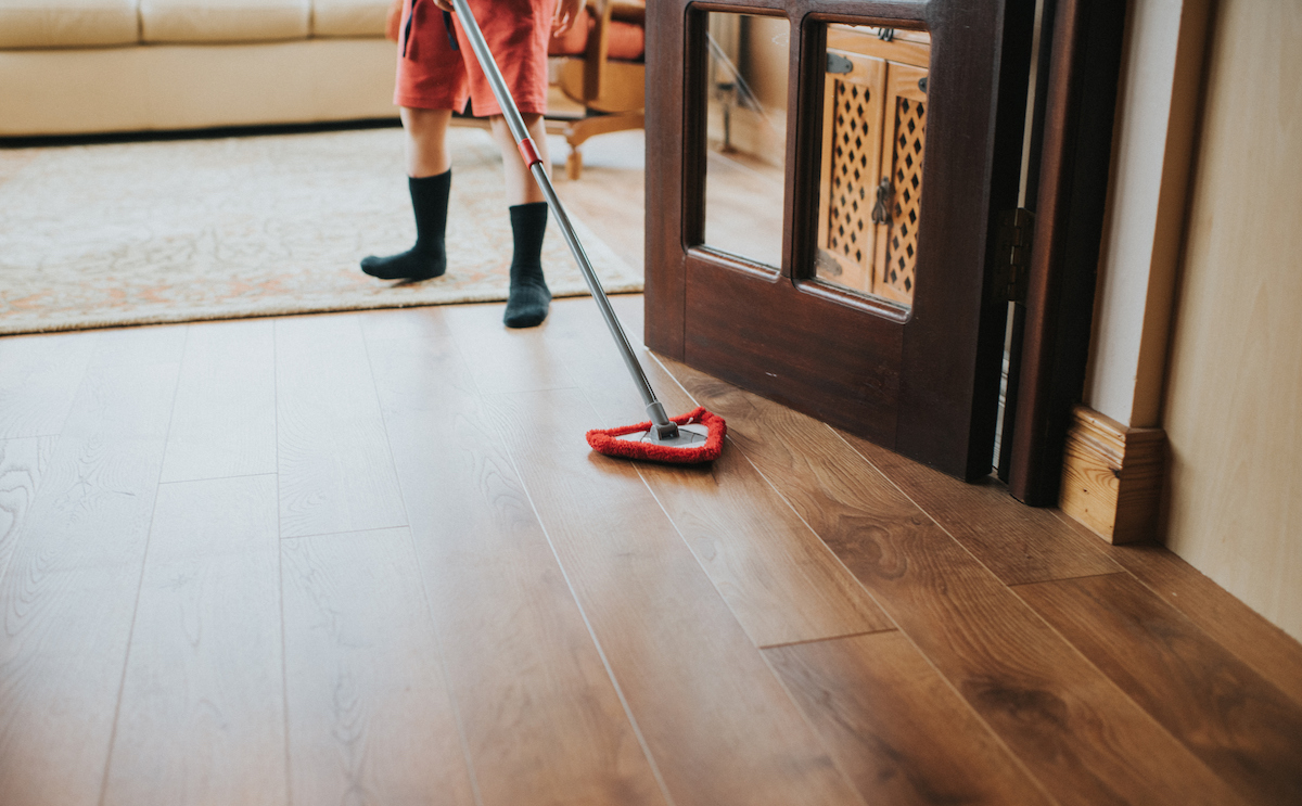 A young person is using a dry mop to clean hardwood flooring.