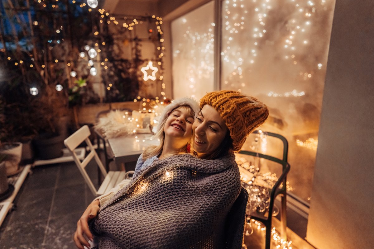 Young girl wearing winter hat and her mom wearing winter hat smiling and enjoying time together on the decorated patio.