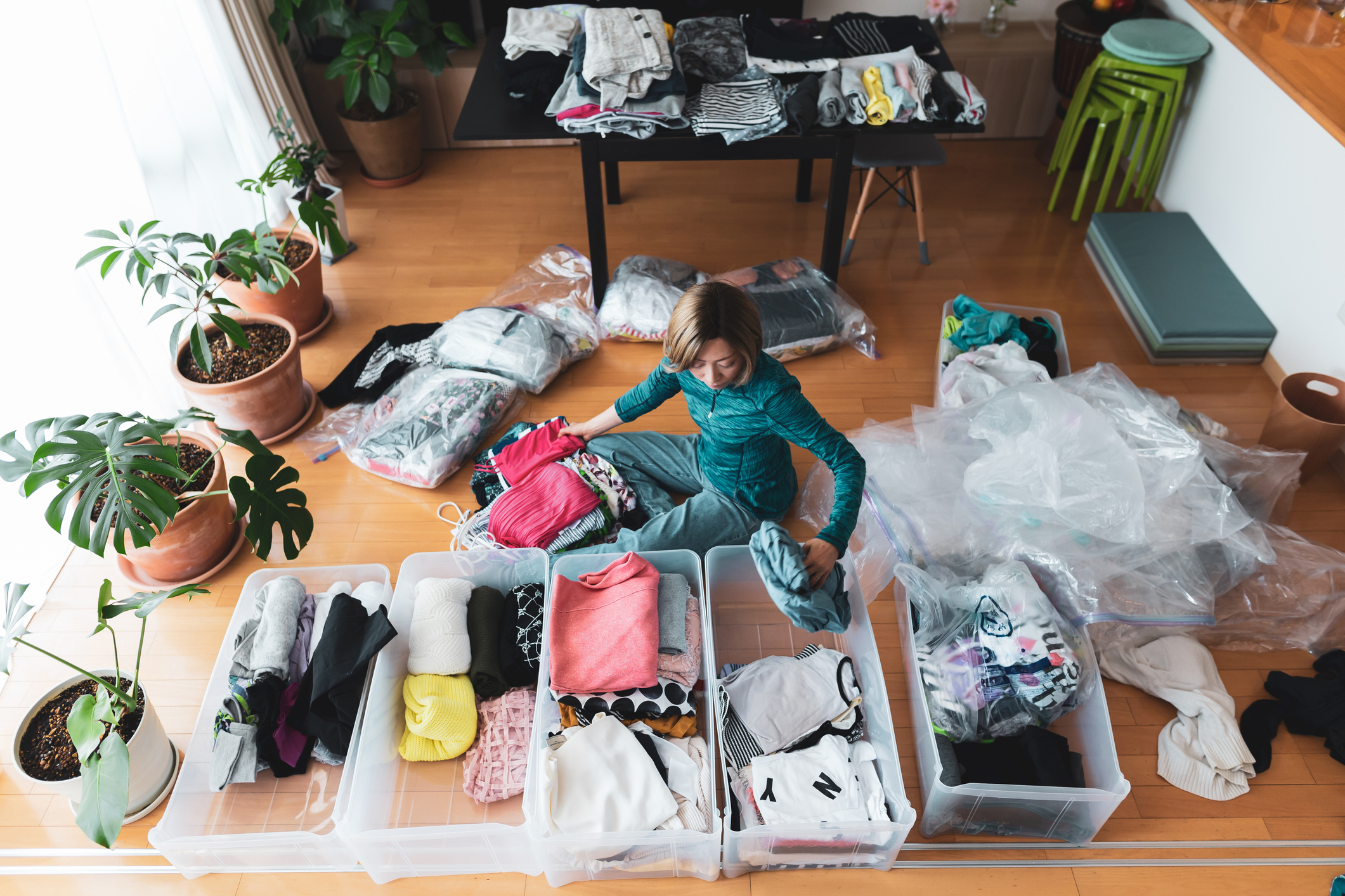 Woman organizes clothes into plastic bins on the floor in her living room.