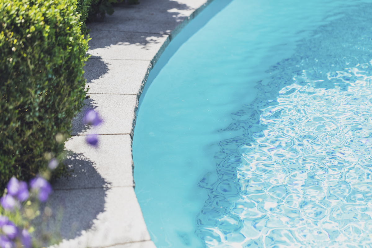 A flowering garden lines the stone edge of a swimming pool.