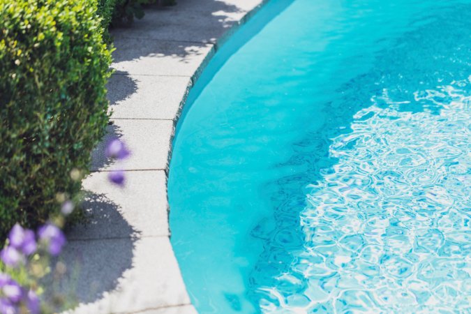 A flowering garden lines the stone edge of a swimming pool.