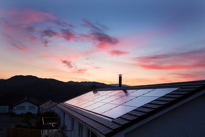 Built in solar panels on a house roof during a beautiful pink and orange sunset.