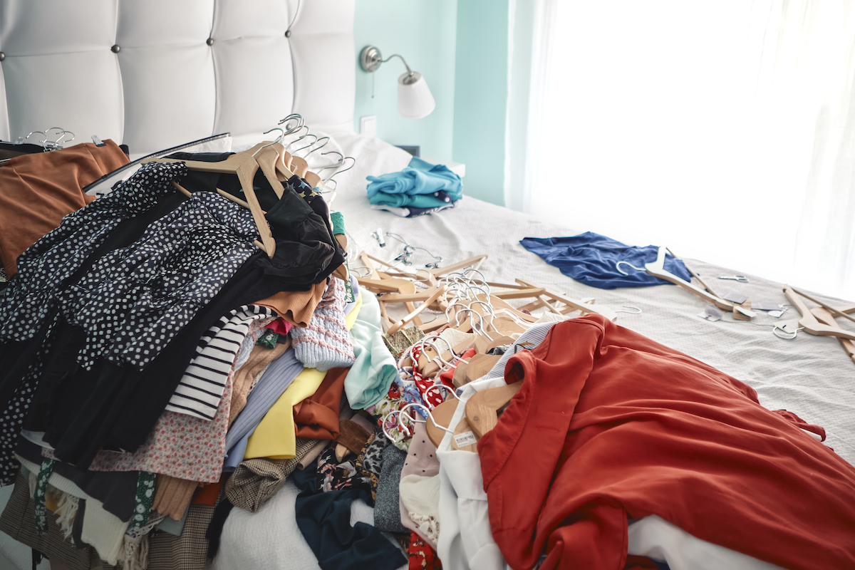 Clothes on hangers are stacked on top of a bed to prepare for closet organization.