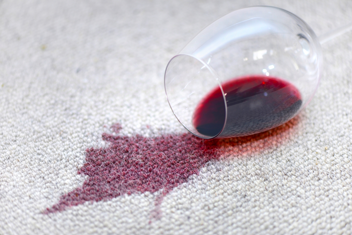 Glass of red wine spilled on white carpet.