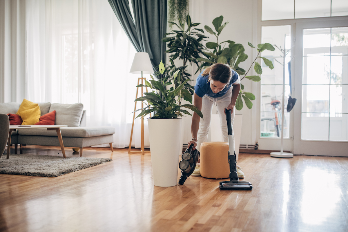 A woman is using the attachments of a wireless vacuum to clean hardwood flooring.