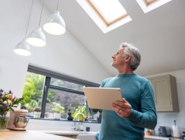 A man is using a tablet to dim the lights in the kitchen.