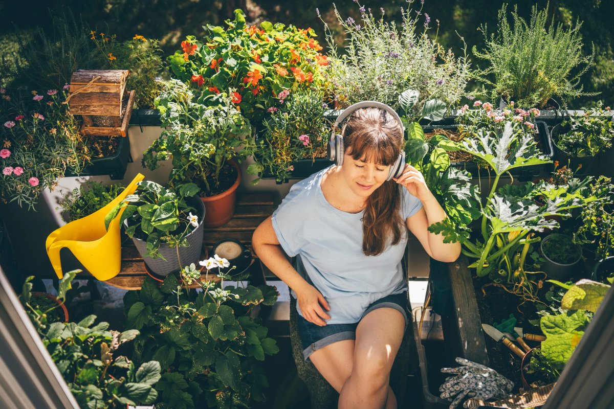 Smiling woman listening to music with wireless headphones near plants in garden.