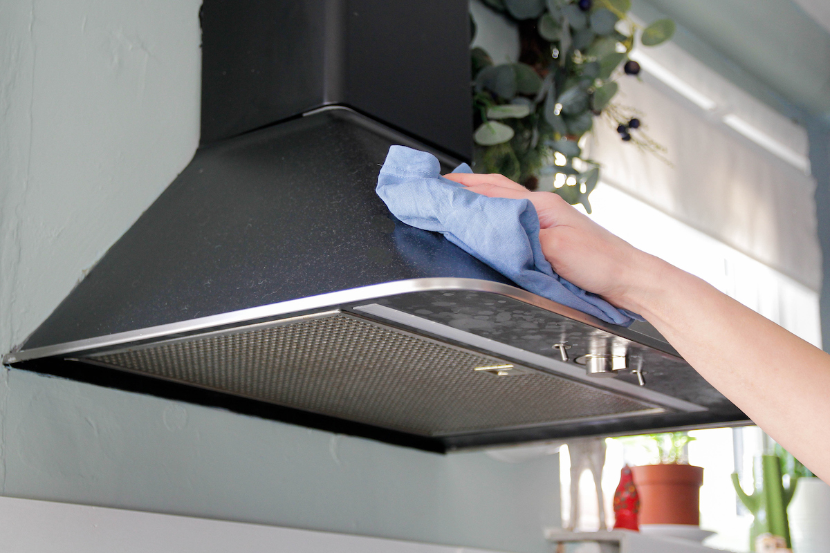 A person is using a microfiber cloth to clean the top of a range hood.