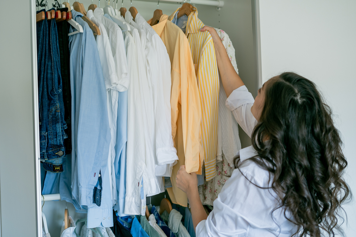 A woman is organizing shirts in a closet by color and sleeve length.