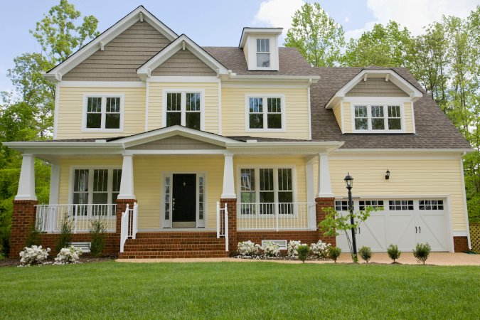 A yellow two-story home features manicured landscaping and a clean exterior.