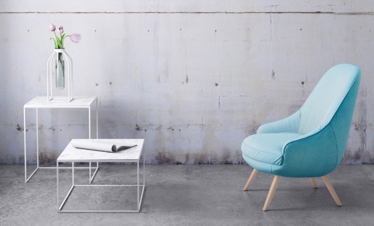 A teal chair and two small white metal tables are placed in a concrete basement room.