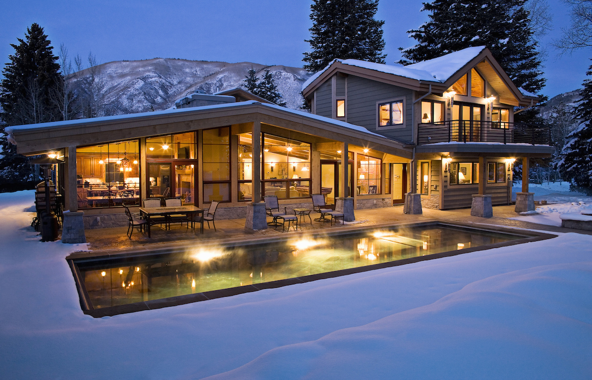 A home in the mountains is covered with snow and features an uncovered inground pool in the backyard.