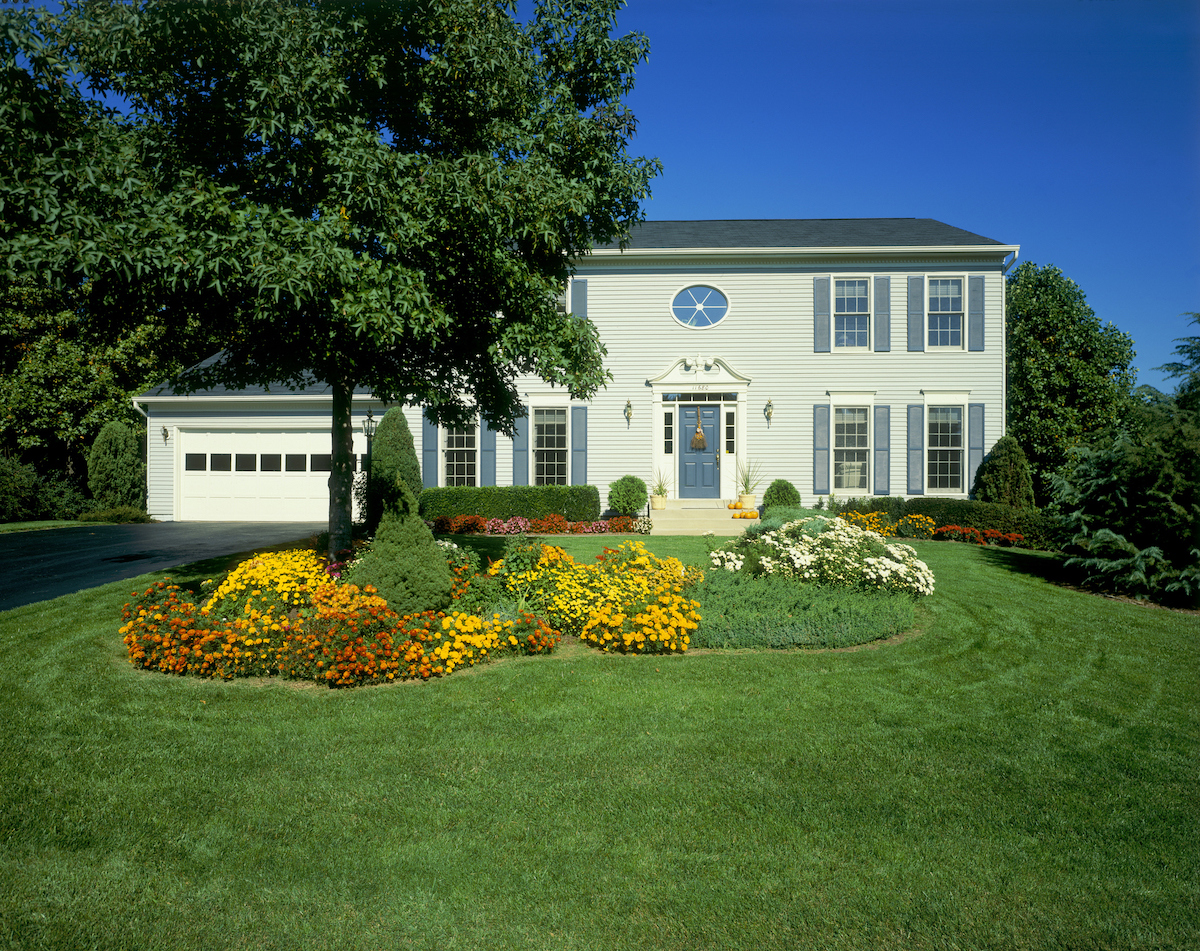 A house with siding and garage has a lawn featuring a tree, landscaped bushes, and manicured lawn.