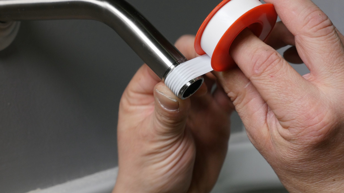 A mature person applies plumber's tape to the male threading of a pipe that will have a shower head screwed onto it.