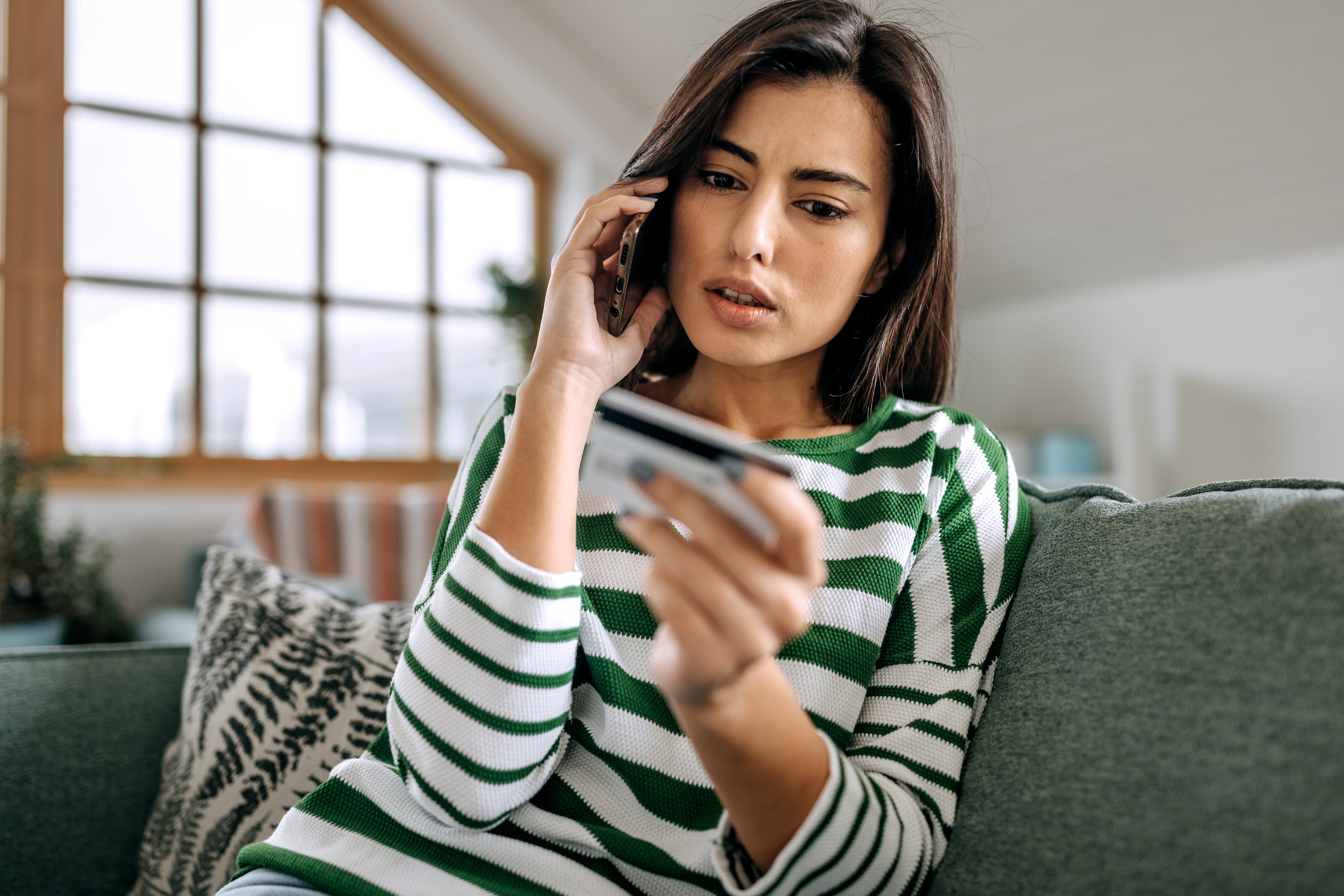 A visibly upset or confused woman is speaking on the phone while looking at her credit card.