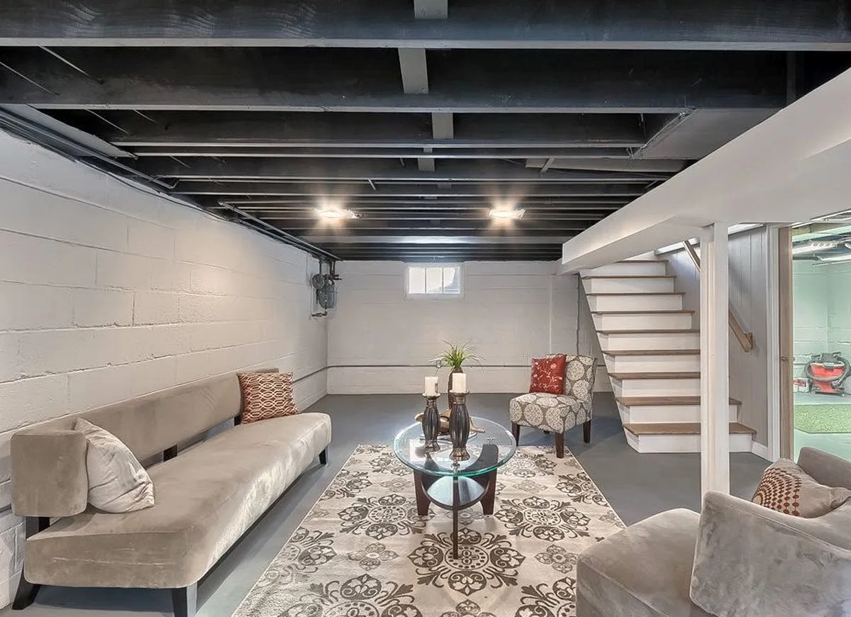 Unfinished basement with painted rafters and furniture.