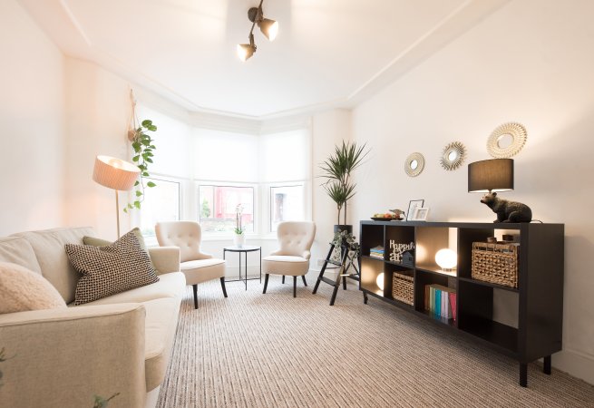 A general interior view of a room with beige sofa, two accent lounge chairs, black sideboard, bookshelves and a new beige carpet.