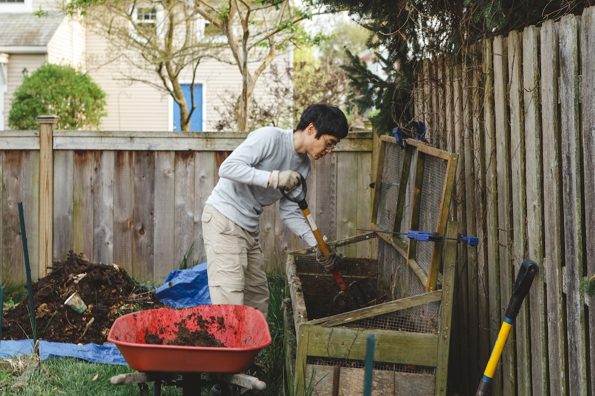 A man in a garden mixes compost in a backyard vegetable garden.