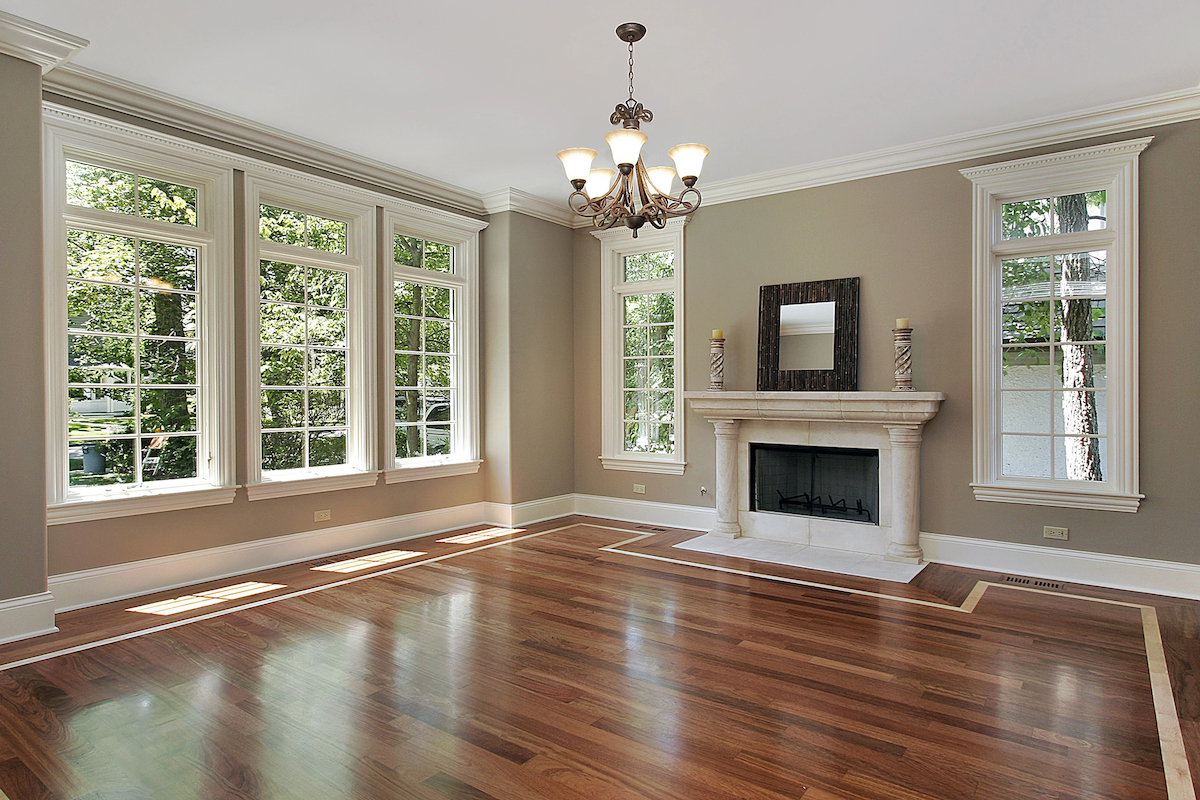 An empty living room in a new construction home features a columned mantel, fireplace, hardwood flooring, and large windows.