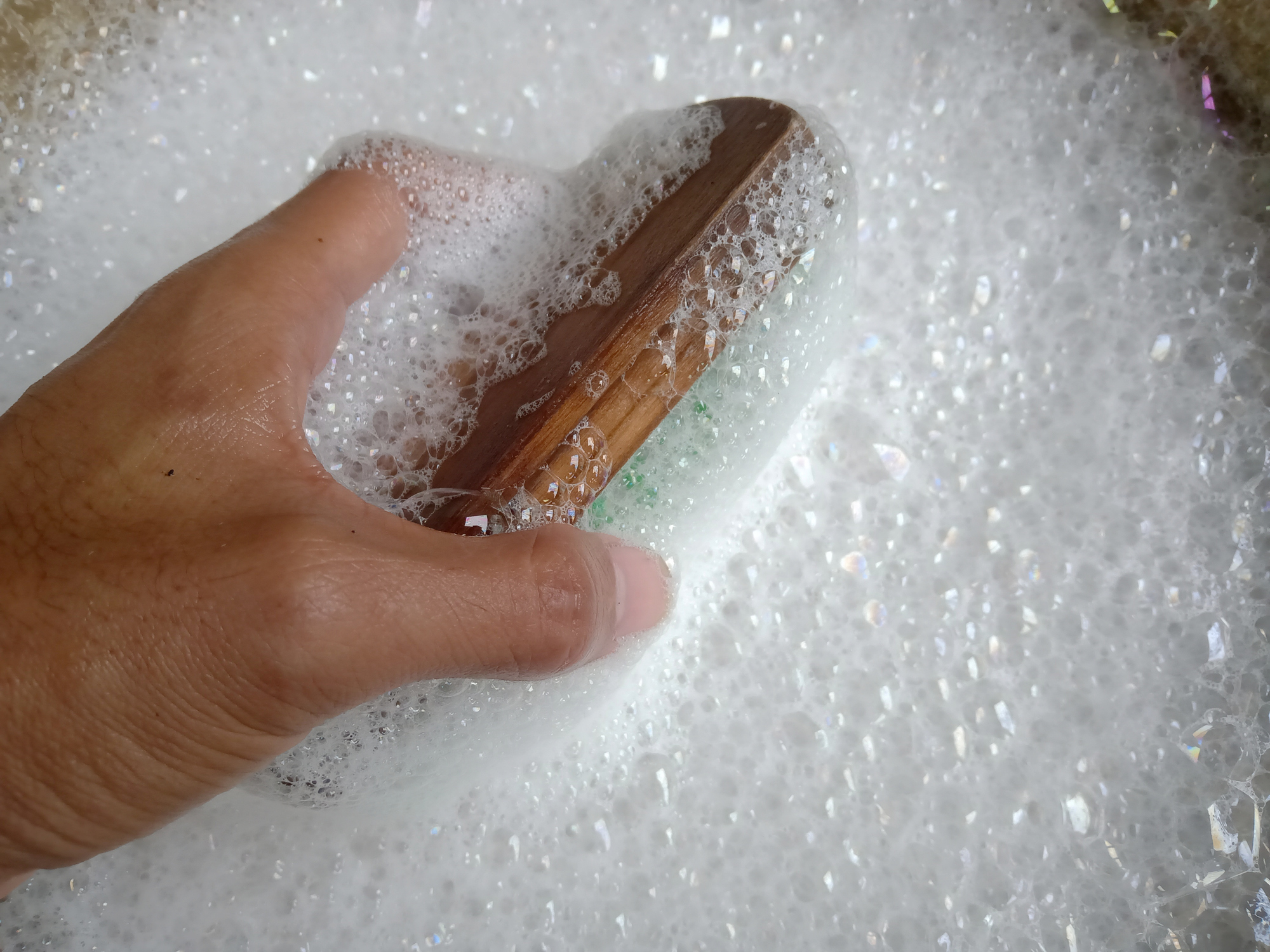 A person dips a soft-bristled brush into a bucket of soapy water.