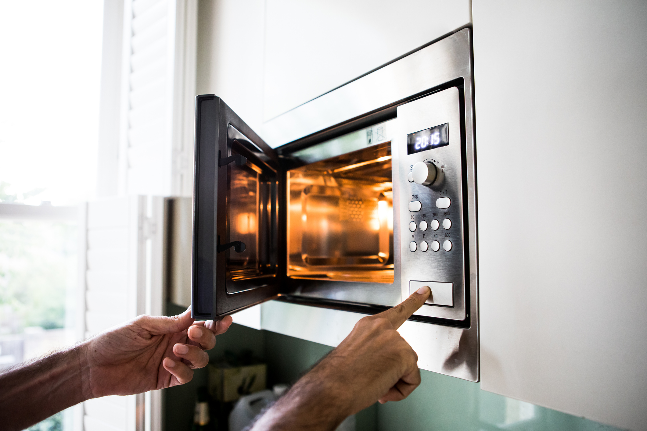 A man using a microwave oven; his finger is on the opening button.