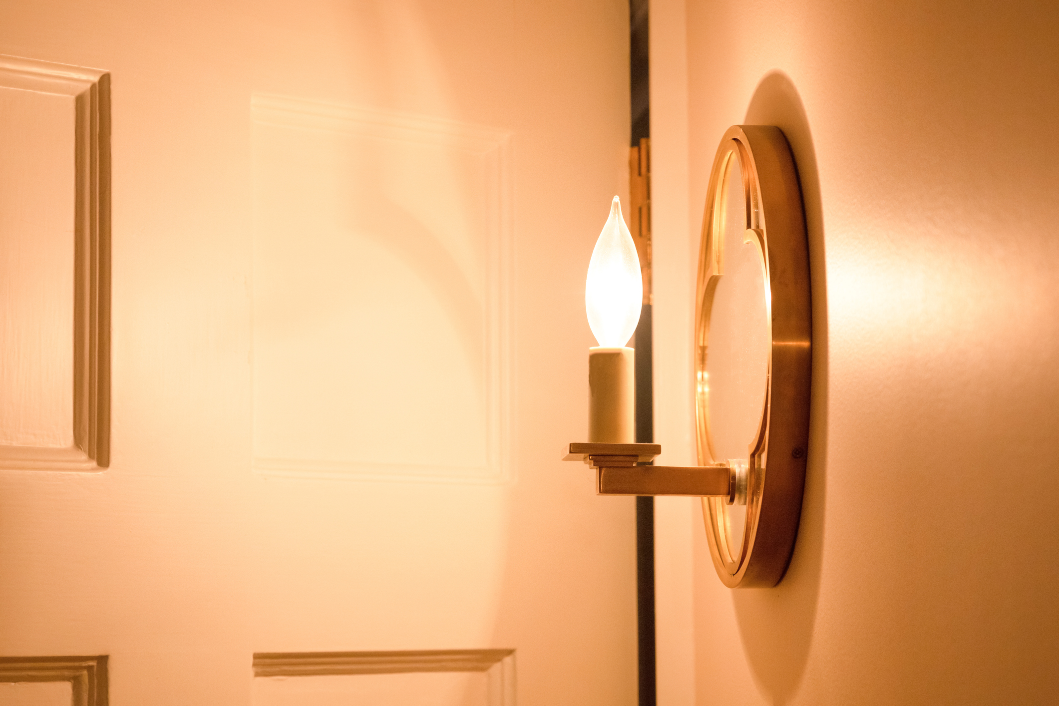 The exposed LED bulb of a wall sconce bathing a corner in warm light.