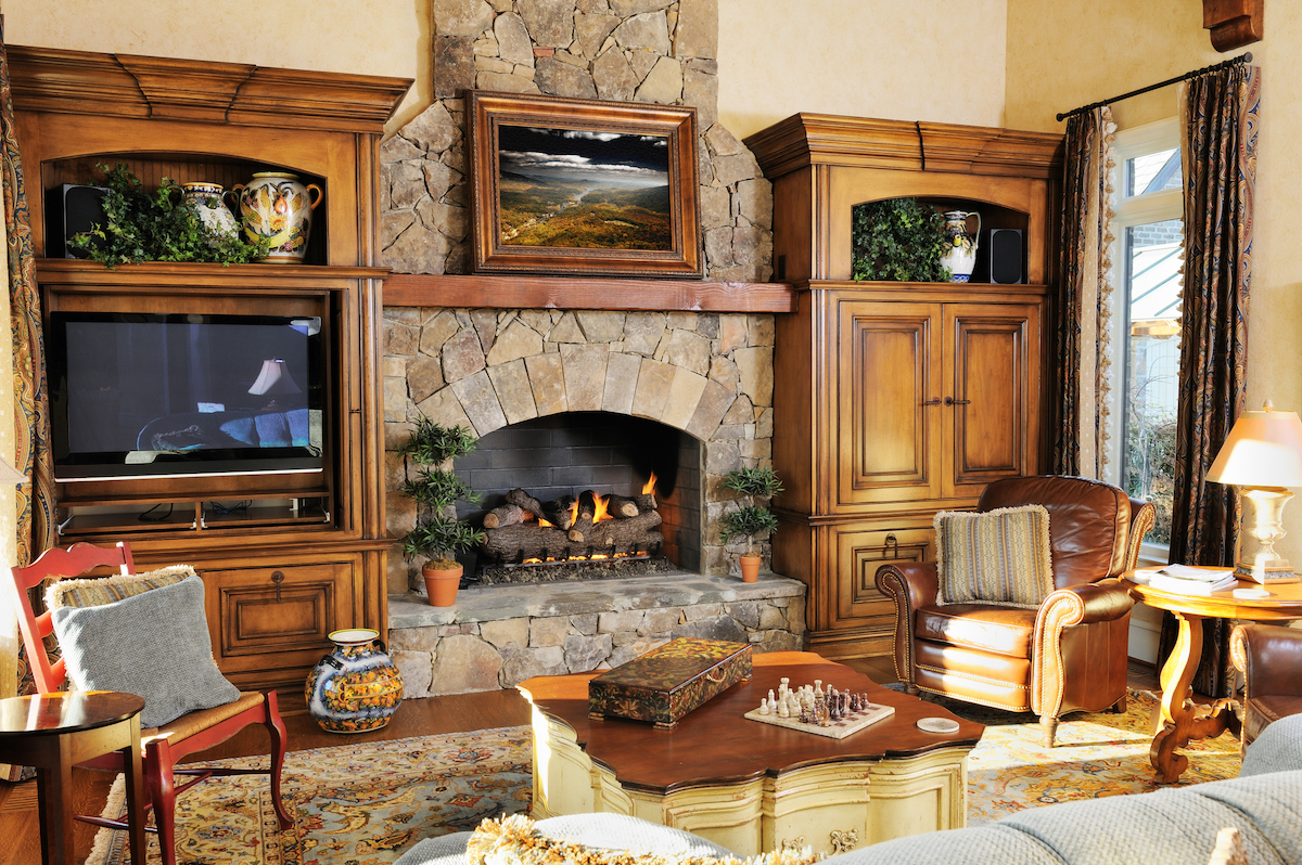 A stone fireplace houses burning logs in a living room decorated with wood furniture.