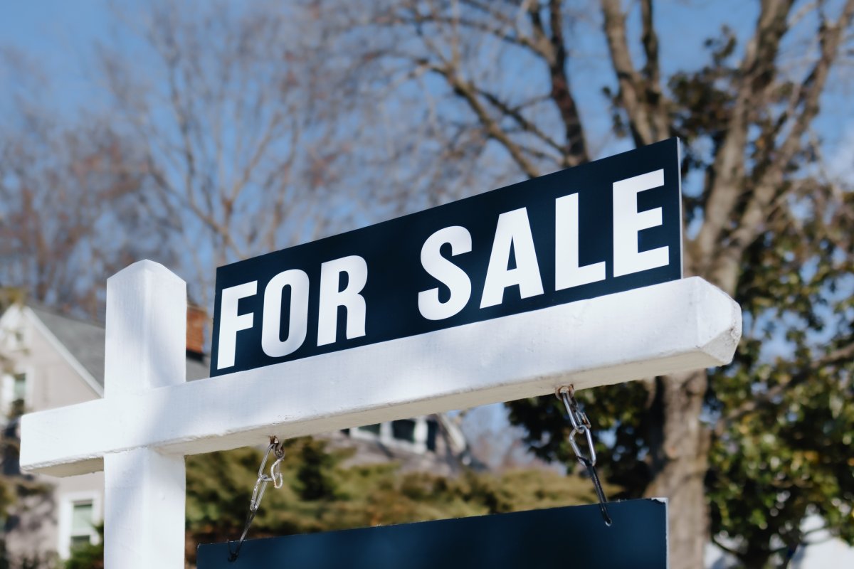 Close-up of a "for sale" sign on post in front yard of house