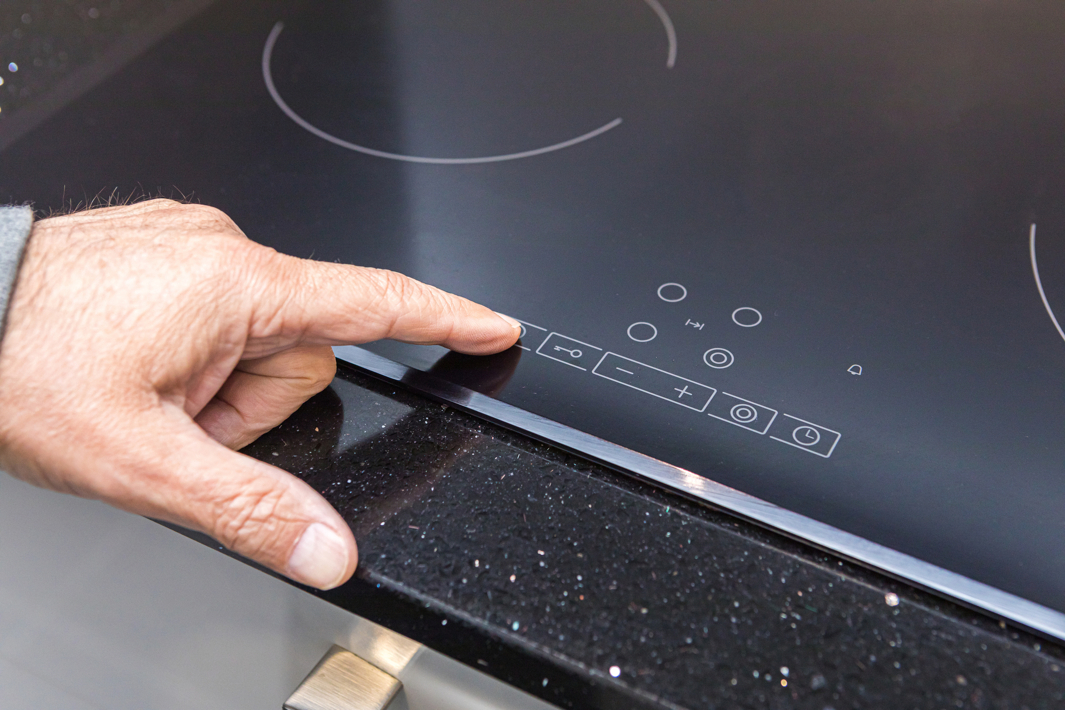 Male hand presses the button on the digital control panel of the induction stove.