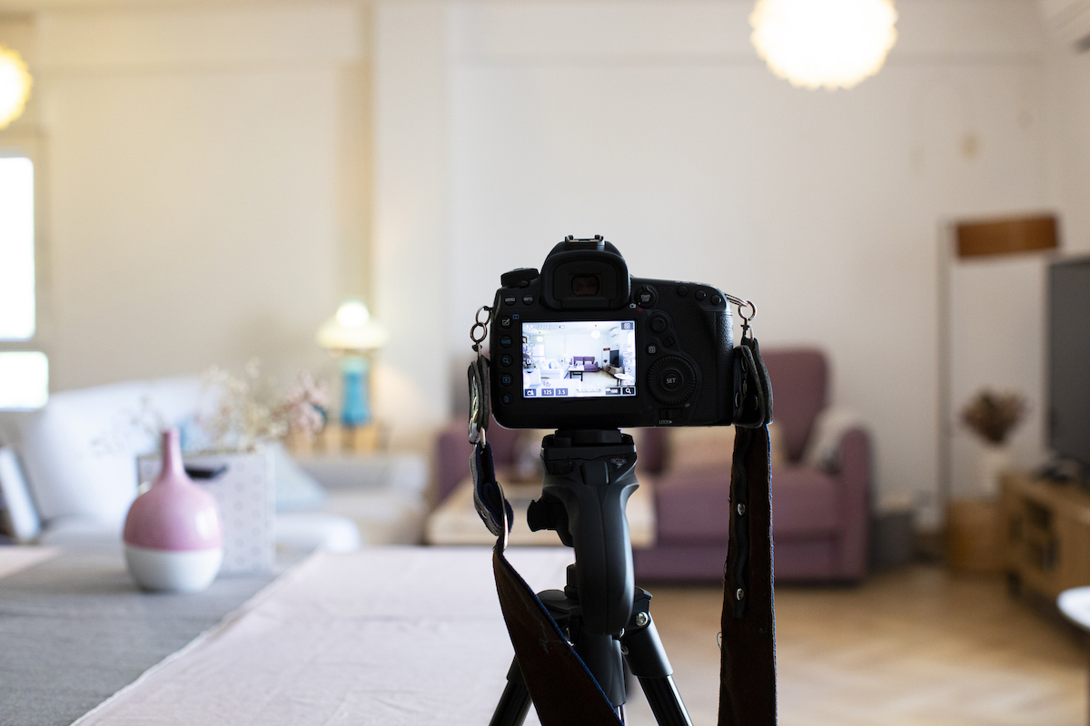 A DSLR camera is set up on a tripod to take photos or videos of a living room.