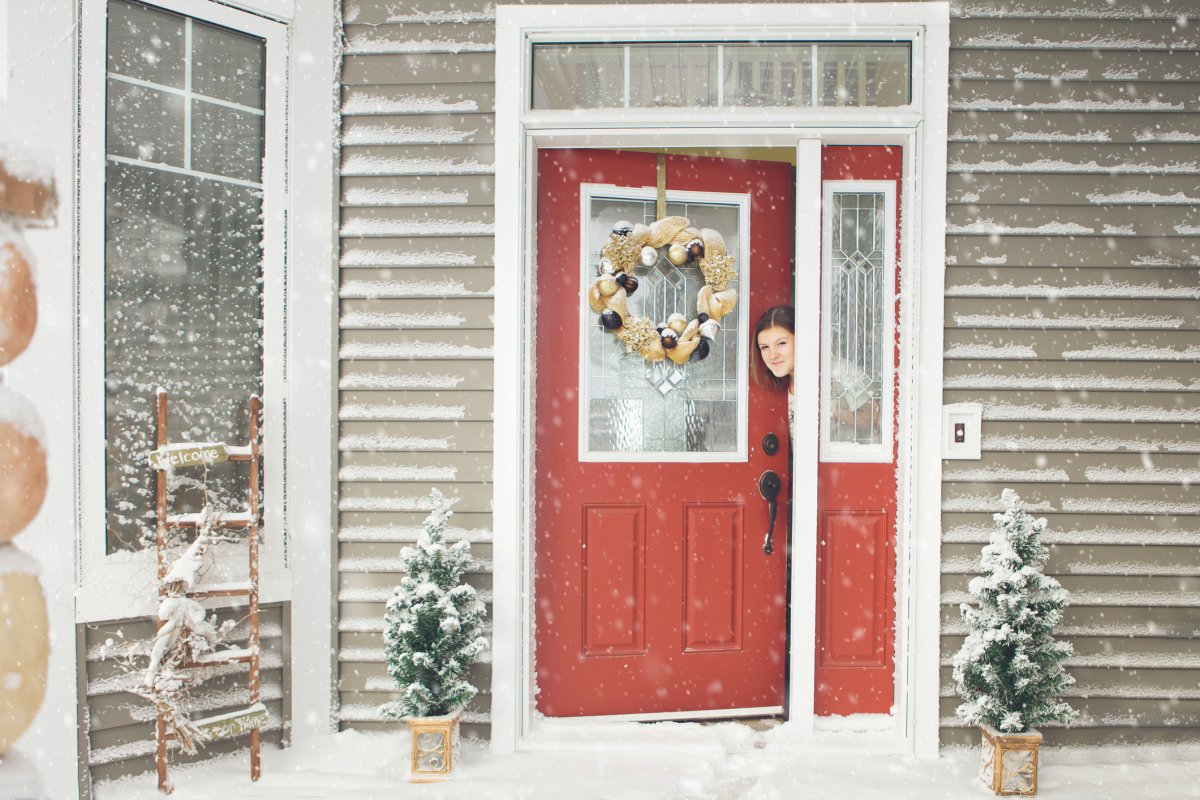 Woman opening red door of her house and seeing snow outside.