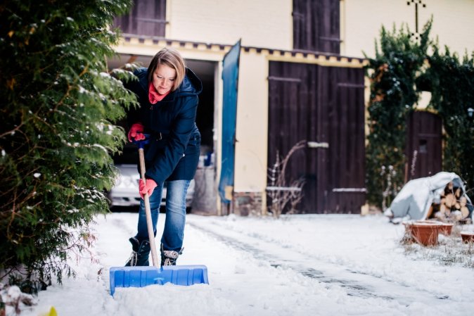 A person shoveling a driveway in front of a house in winter.