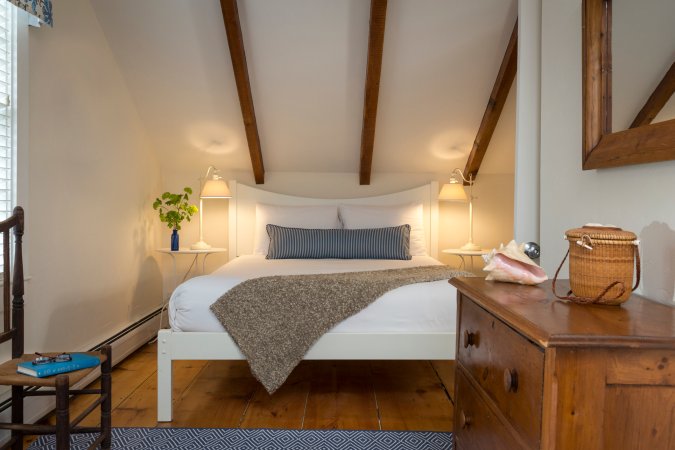 An upstairs spare bedroom furnished with a neatly made bed, two nightstands, dresser, and an extra chair.