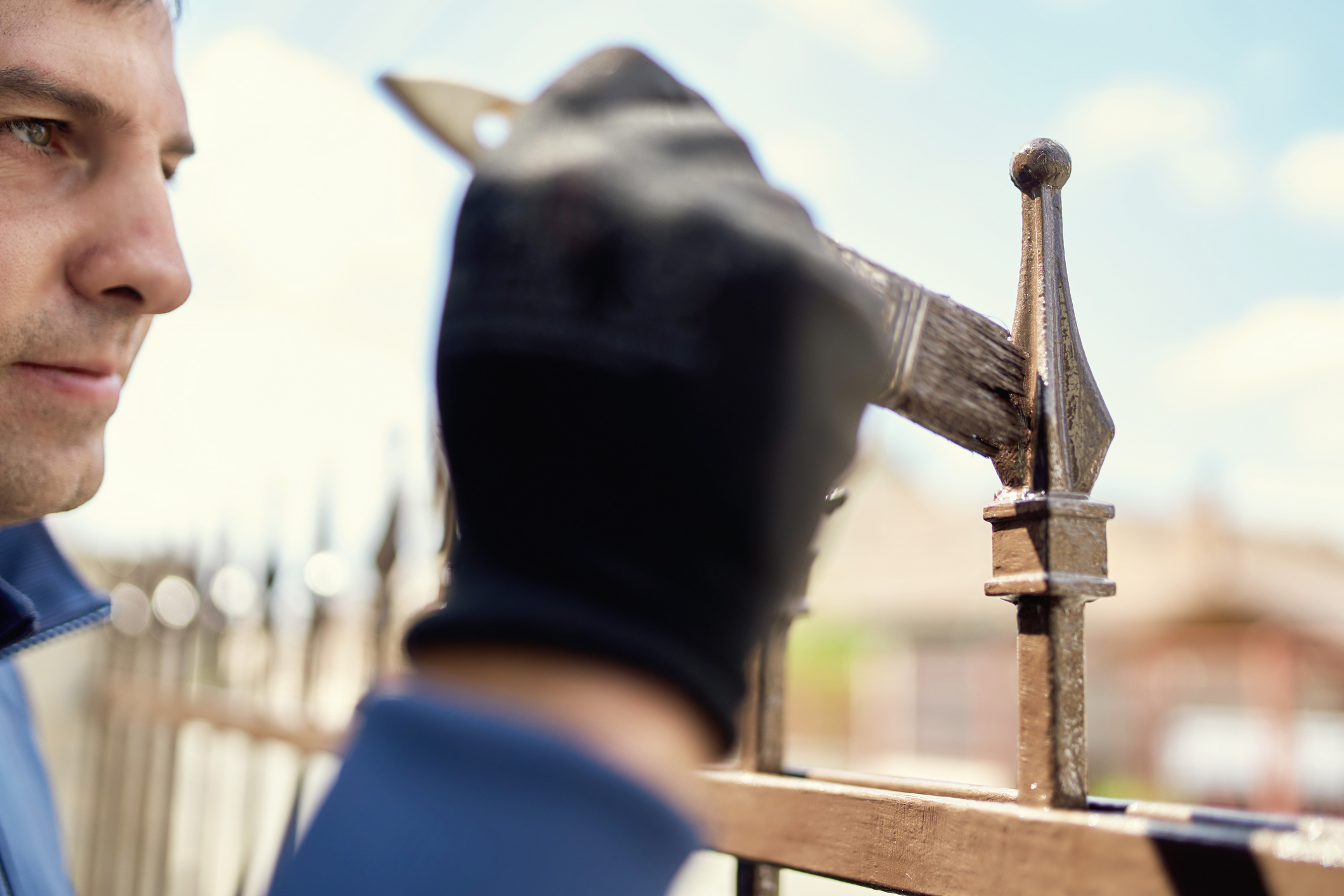 A man brushes an unknown coating onto the top of a clean wrought iron fence post.