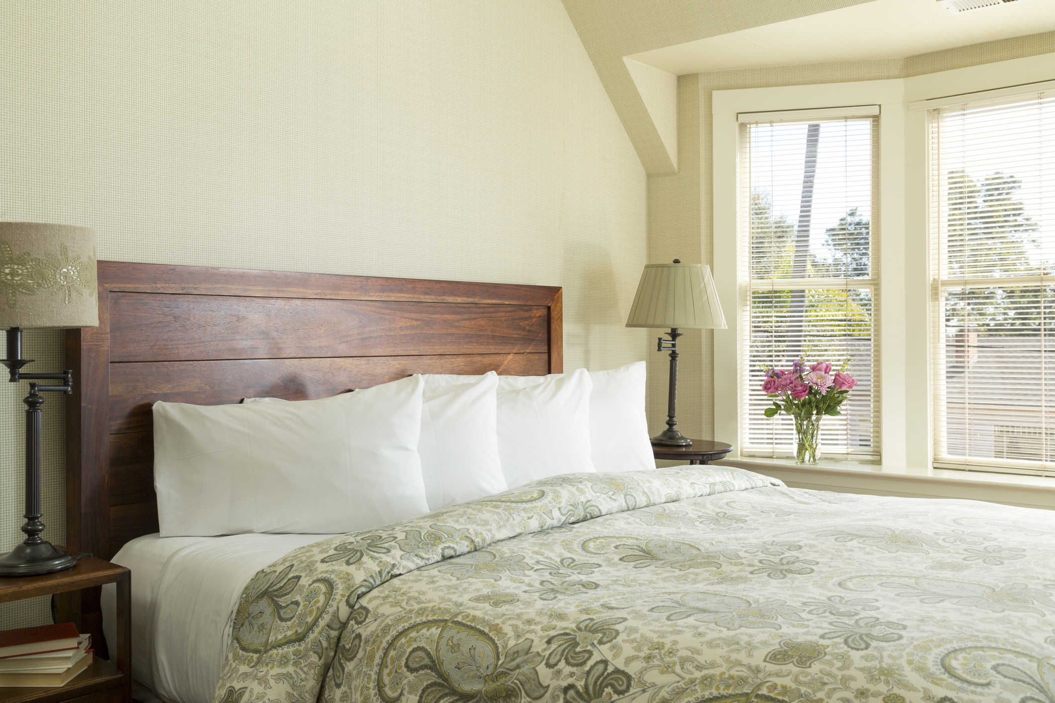 A small upstairs guest bedroom with a window and full-size bed made with a pale-green comforter and four down pillows.