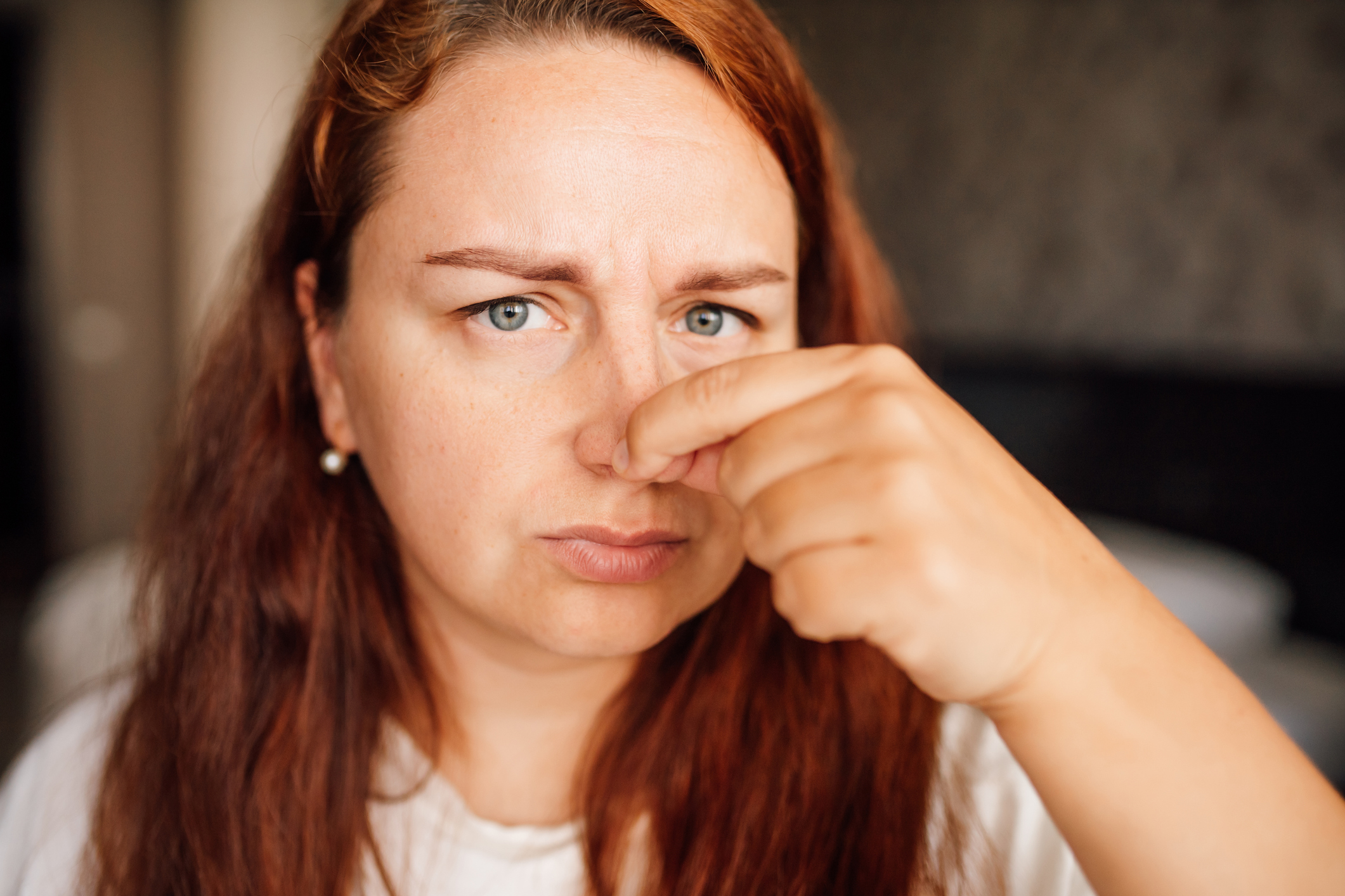 A woman with red hair pinches her nose shut to avoid breathing in a bad odor inside her home.