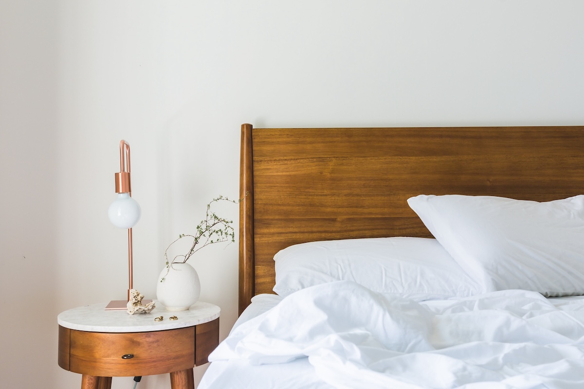 A white and airy bedroom with a wooden headboard and marble-topped nightstand.