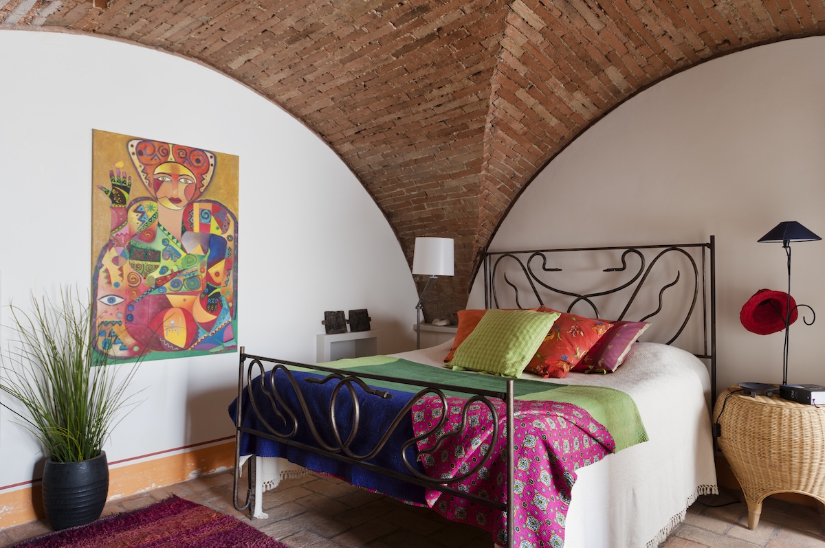 A bedroom with high wood paneled ceilings and bright artwork.