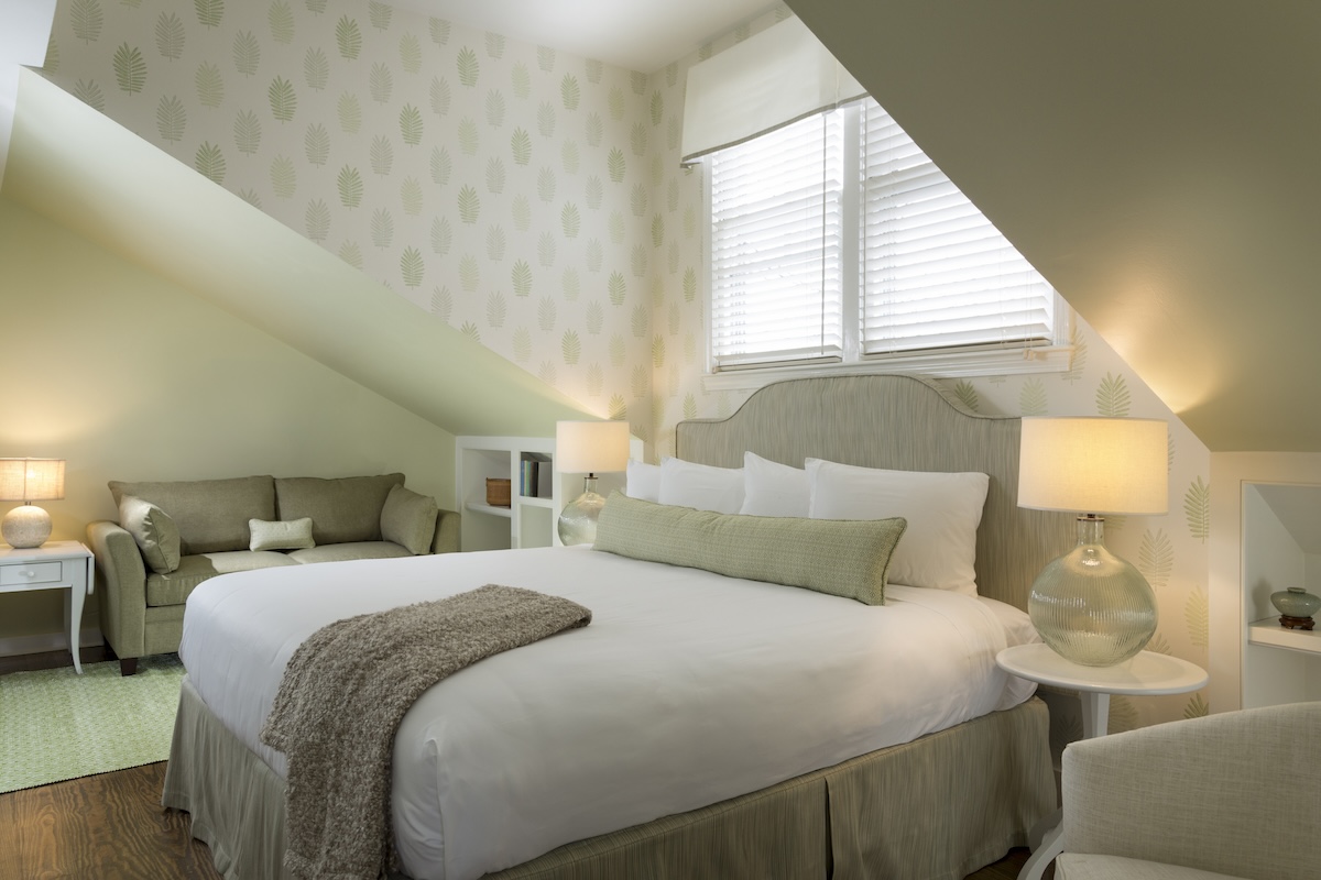 A bedroom with a green color scheme, sitting area, and vaulted ceilings.