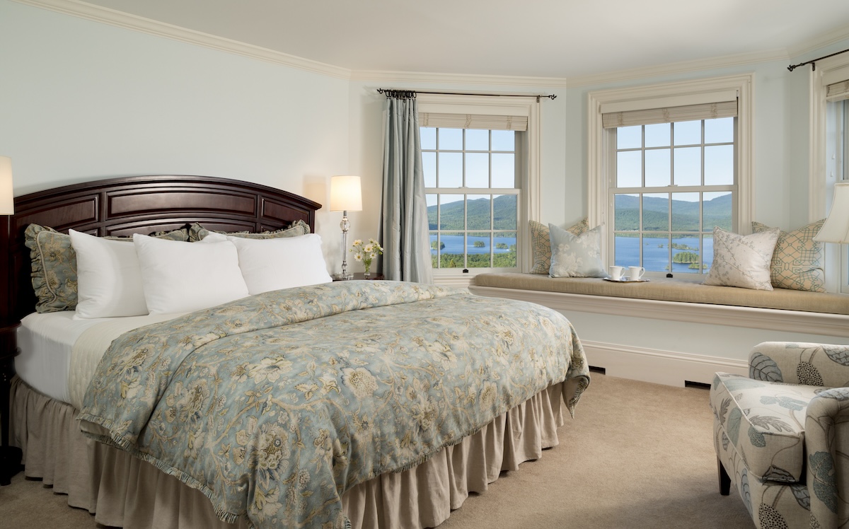 A bedroom with light color scheme and large windows looking onto a lakefront view.