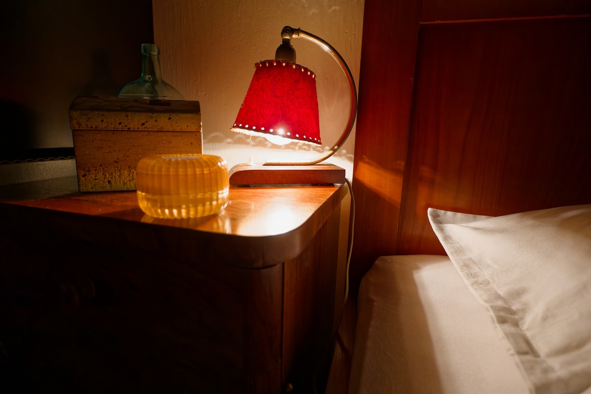 Small bedside lamp with red lampshade on a bedside table.