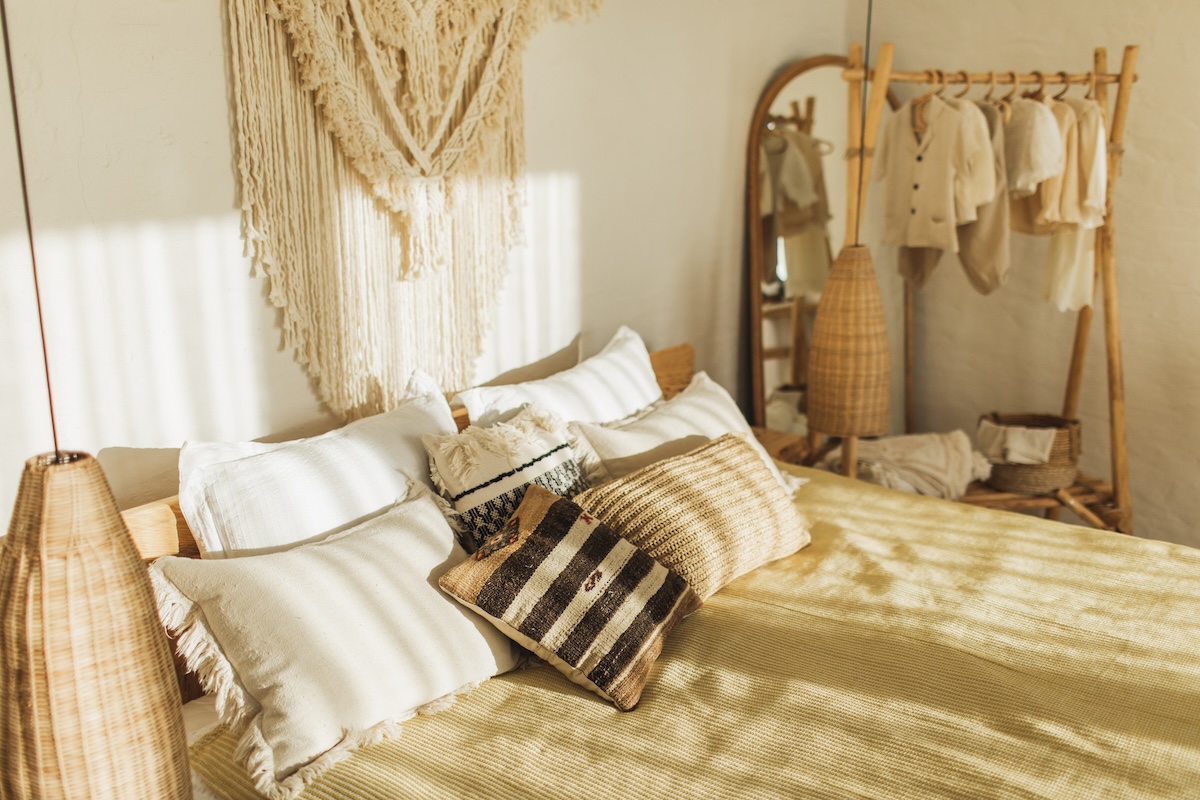 A bohemian styled bedroom with white linens and beige pillows.