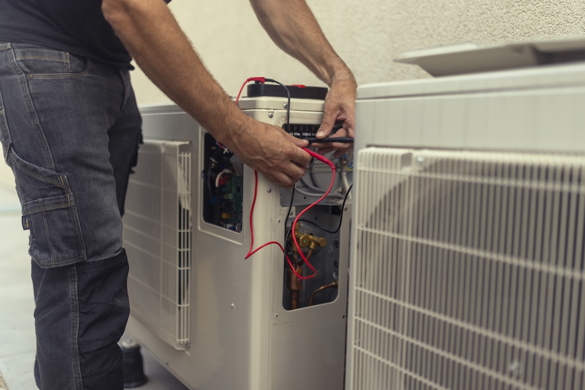 A repair person repairs the wiring on a white exterior heat pump.