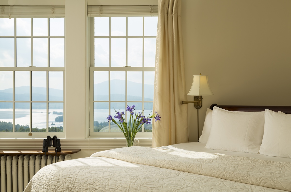 A guest bedroom with a white quilt and vase of flowers near an open window.