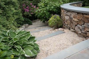 Hardscaping stairs in a backyard with a stone wall and foliage.