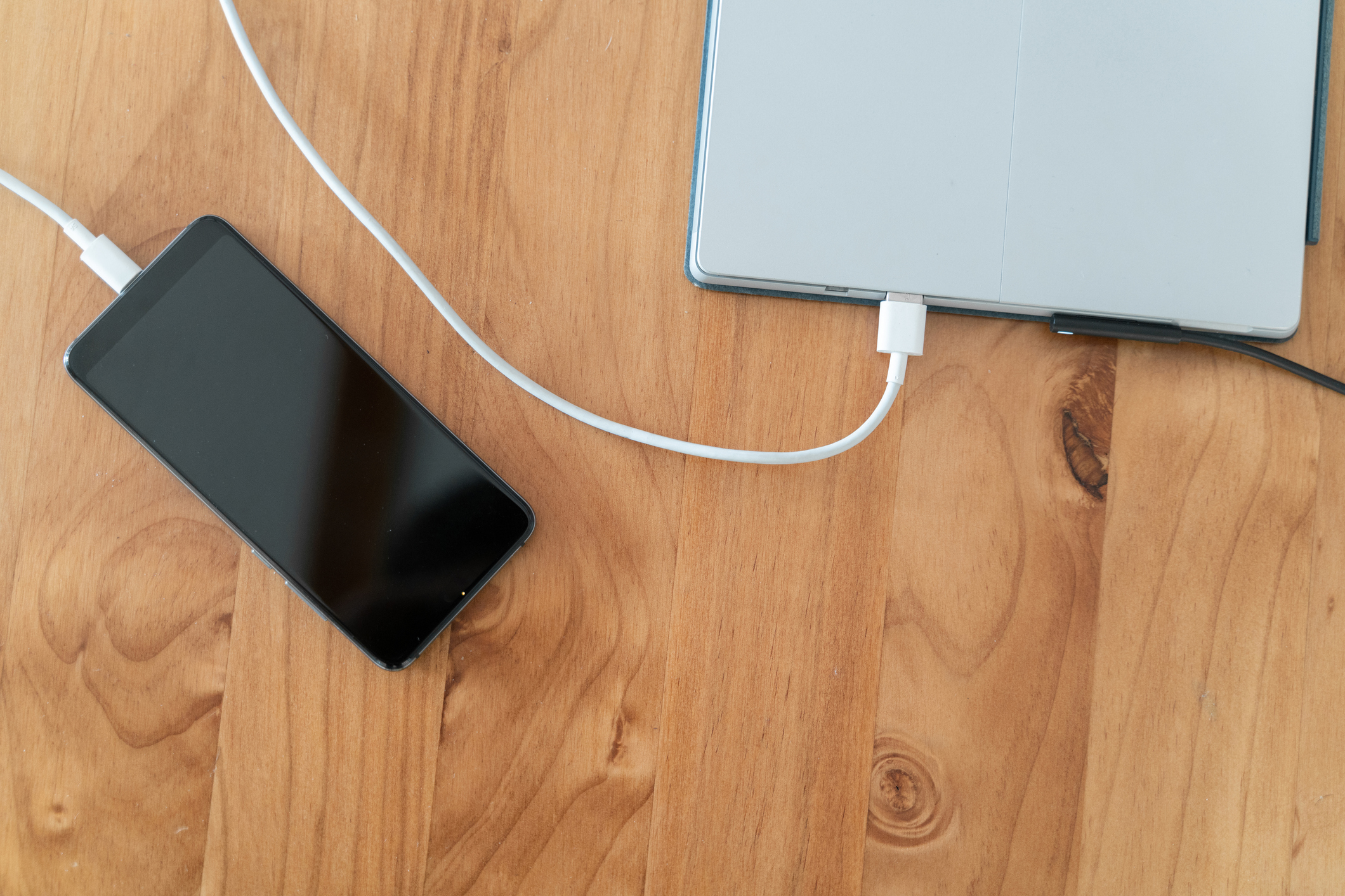 An Apple iPhone and iPad charging on the surface of an oak table.