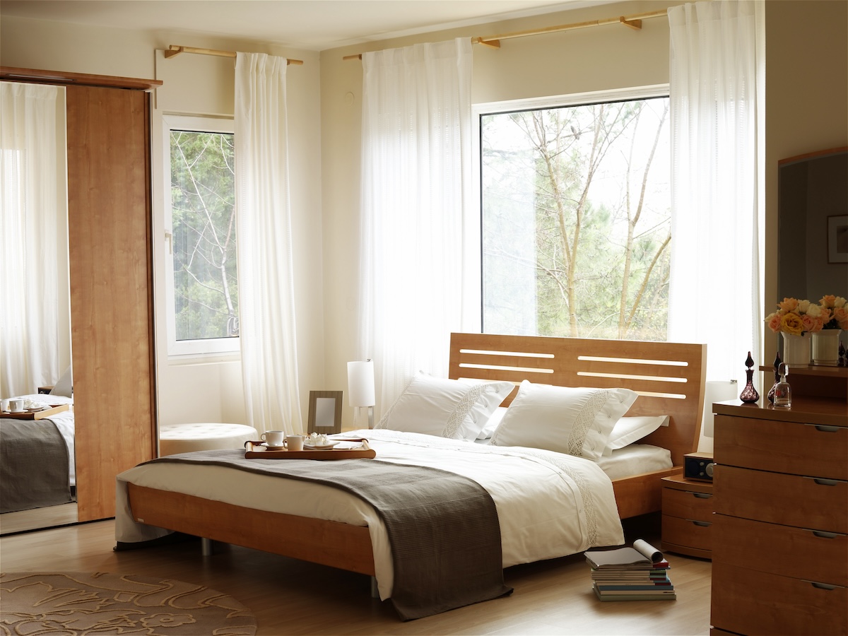 A bedroom with light wooden accents and large windows.