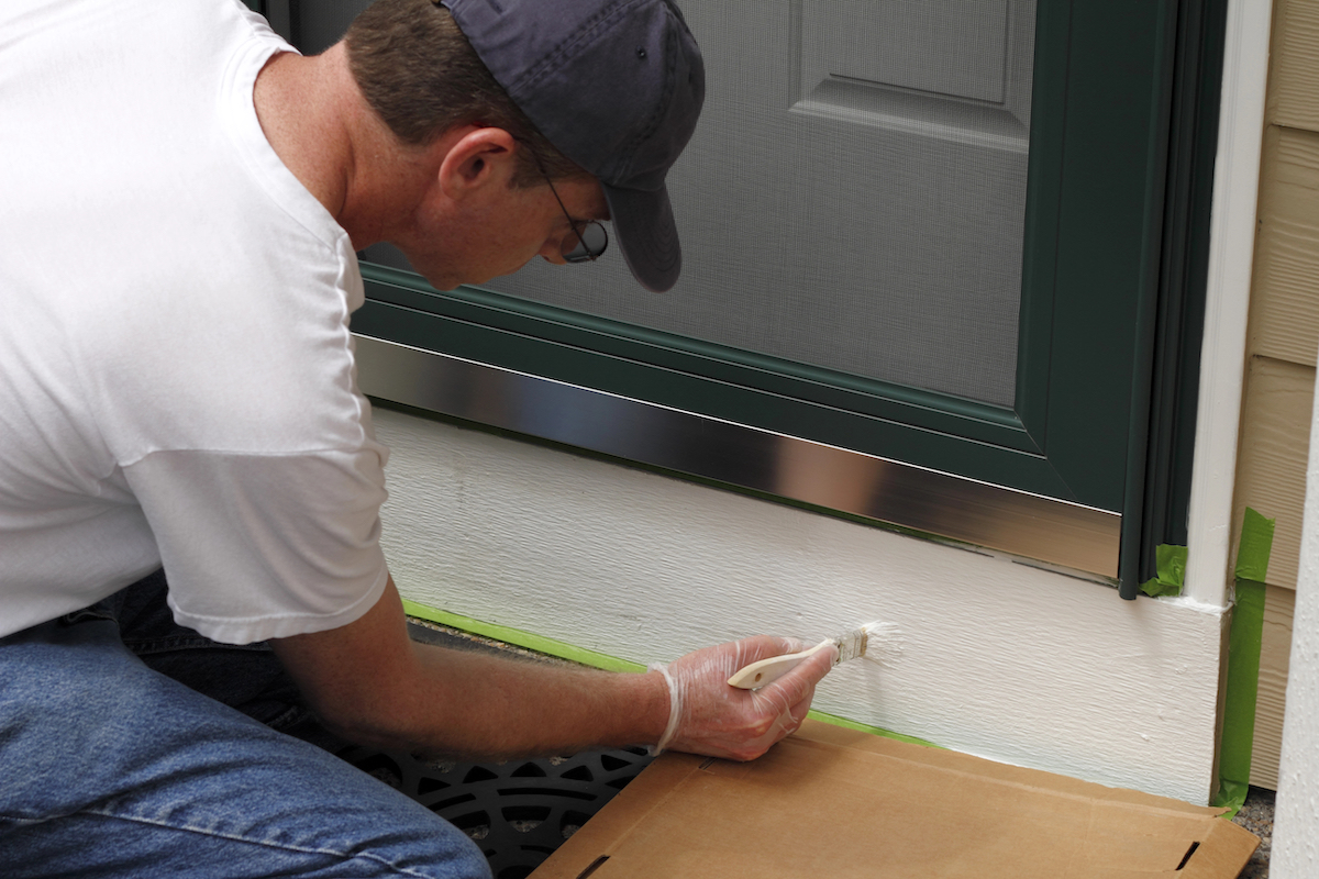 Adult male painting the white part below the front door of his home to make the entry way more inviting and better looking.